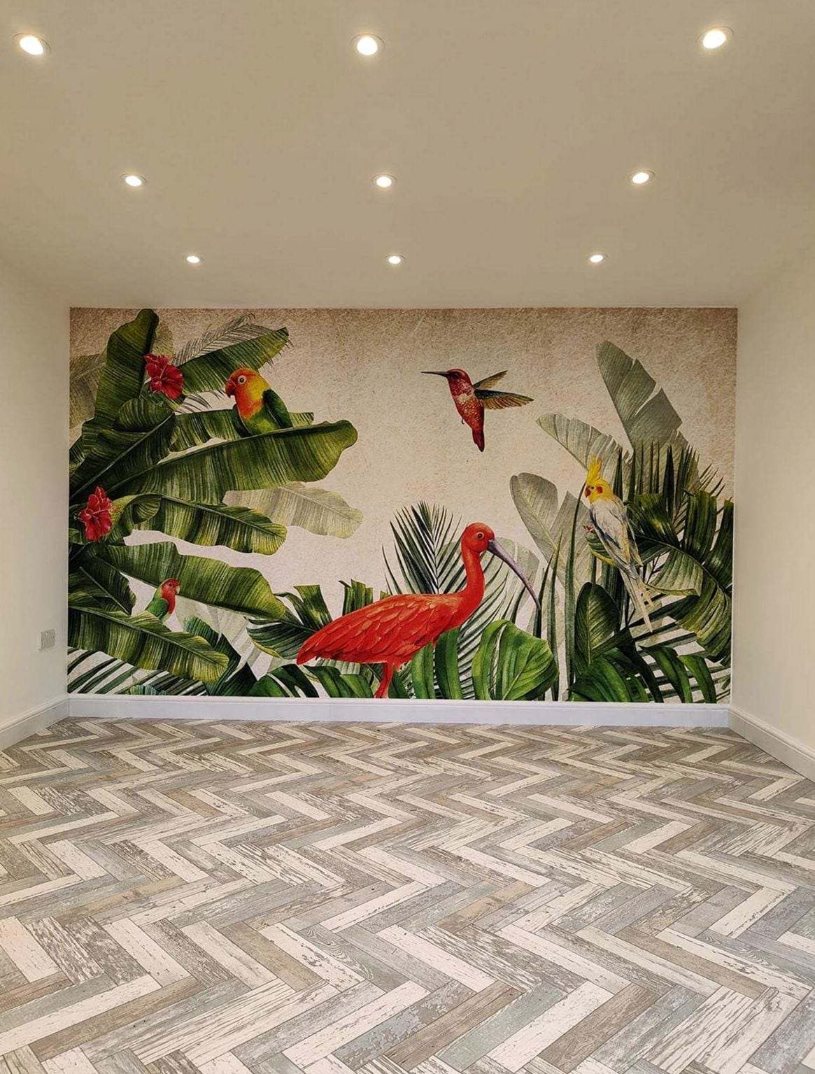 Empty room with a grid of recessed ceiling lights switched on, a tropical mural on the back wall and a herringbone floor