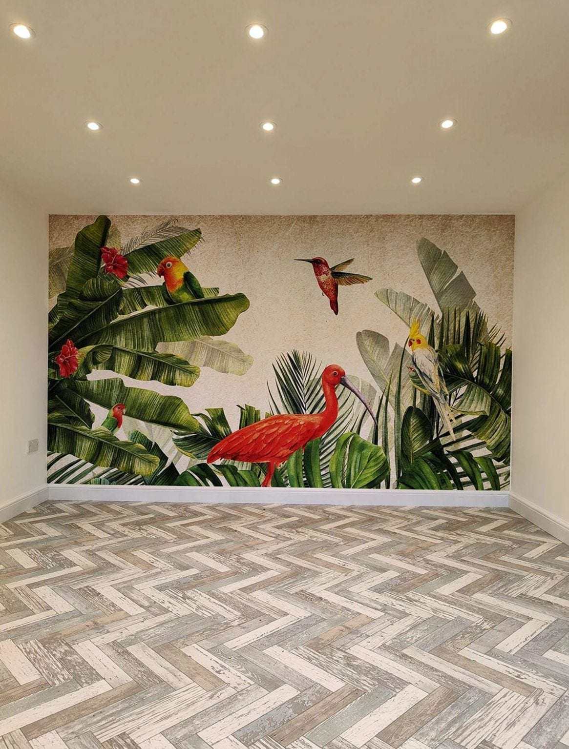 Empty room with a grid of recessed ceiling lights switched on, a tropical mural on the back wall and a herringbone floor