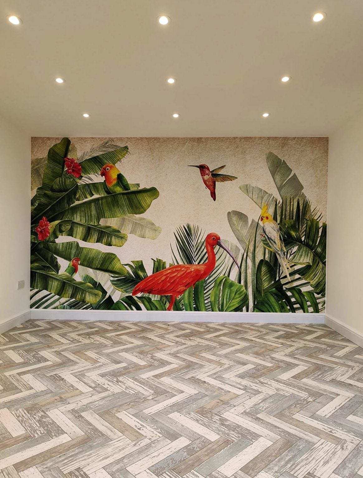 Empty room with a grid of recessed ceiling lights switched on, a tropical mural on the back wall and a herringbone floor