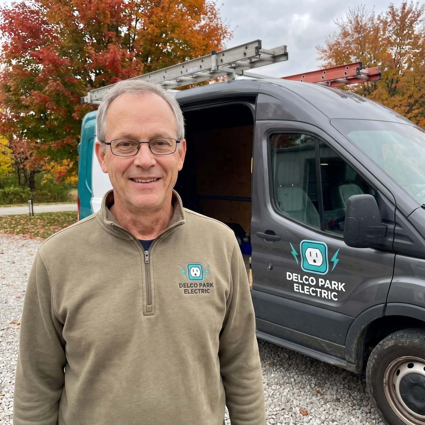 Hugo Kim in a khaki pullover with the Delco Park Electric logo, standing beside the company van